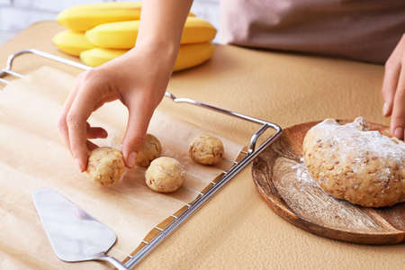 Woman cooking banana cookies on color background