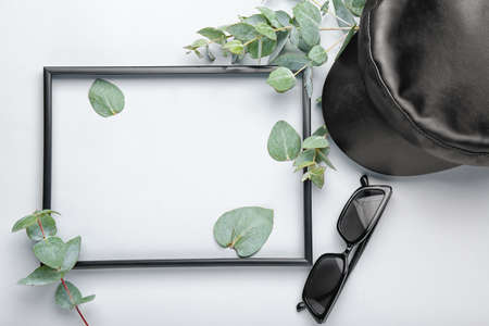Empty frame with eucalyptus leaves and female accessories on light background