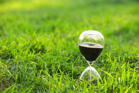 Stylish hourglass on grass outdoors
