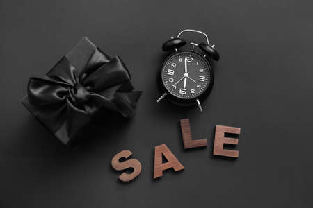Gift box, text SALE and alarm clock on dark background