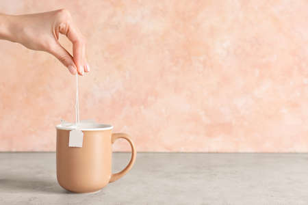 Woman dipping tea bag into cup on color backgroundの写真素材
