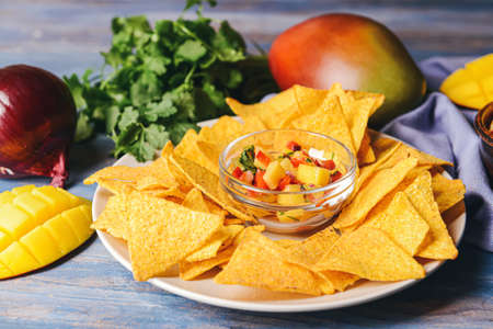 Plate with nachos and fresh mango salsa on color wooden backgroundの写真素材