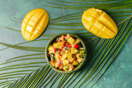 Bowl with fresh mango salsa and tropical leaf on color backgroundの写真素材