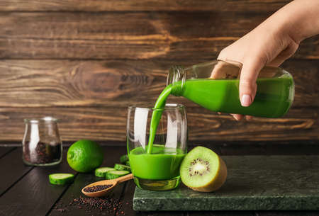 Woman pouring green smoothie from bottle into glass on dark wooden backgroundの写真素材