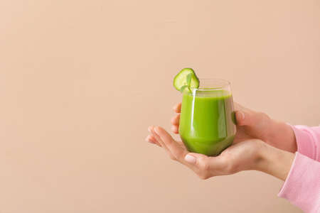 Woman holding glass of healthy green smoothie on color background