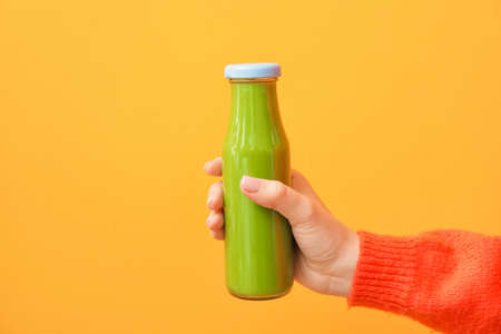 Woman holding bottle of healthy green smoothie on color backgroundの写真素材