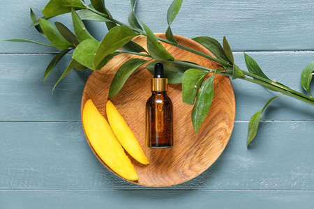 Plate with bottle of mango essential oil on color wooden backgroundの写真素材