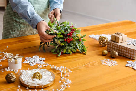 Woman making composition with mistletoe branches on tableの写真素材