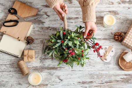 Woman making composition with mistletoe branches on tableの写真素材
