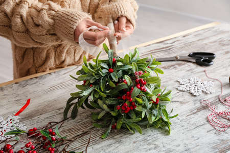 Woman making composition with mistletoe branches on tableの写真素材
