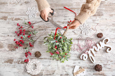 Woman making composition with mistletoe branches on tableの写真素材