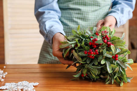 Woman making composition with mistletoe branches on tableの写真素材