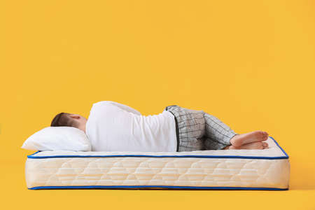 Young man lying on soft mattress against color backgroundの写真素材