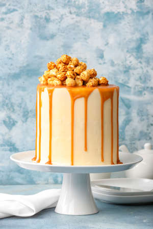 Tasty cake with popcorn and caramel on color background