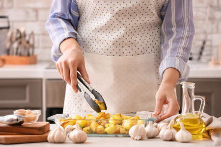 Woman cooking potatoes with garlic on table in kitchenの写真素材
