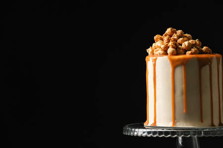 Tasty cake with popcorn and caramel on dark background