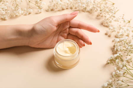 Female hand with jar of cream and beautiful flowers on color backgroundの写真素材