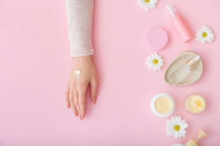 Female hand with cosmetic products and beautiful flowers on color backgroundの写真素材
