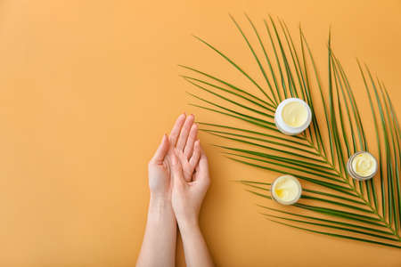 Female hands with jars of cream and tropical leaf on color backgroundの写真素材