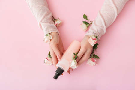 Female hands with cosmetic product and beautiful flowers on color backgroundの写真素材