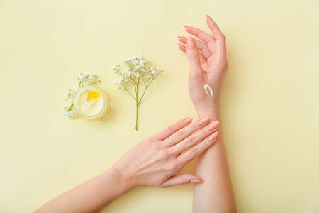Female hands with jar of cream and beautiful flowers on color backgroundの写真素材