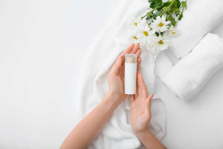 Female hands with cosmetic product and beautiful flowers on light backgroundの写真素材