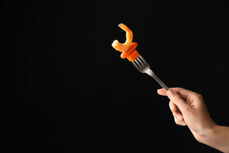 Female hand and fork with shrimp and vegetables on dark backgroundの写真素材