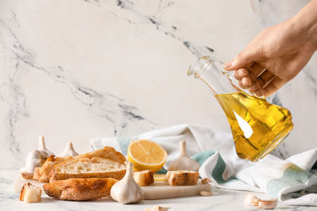 Woman pouring garlic oil onto bread on light background