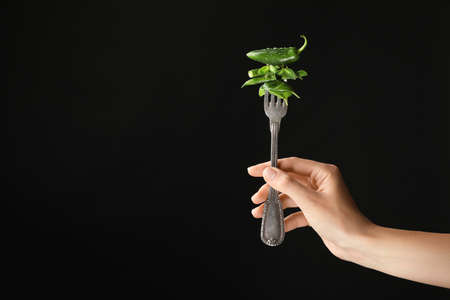 Female hand and fork with pepper and herbs on dark backgroundの写真素材