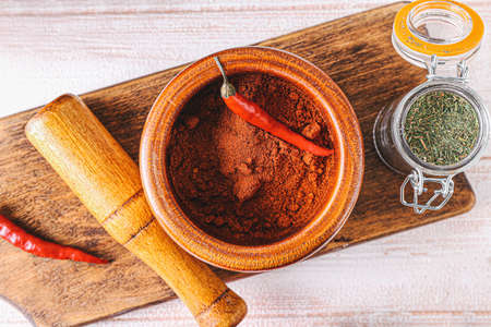 Mortar with chili pepper powder and pestle on light wooden backgroundの写真素材