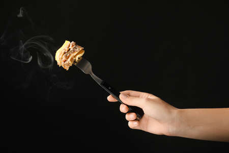 Female hand and fork with lasagna on dark backgroundの写真素材