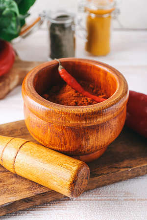 Mortar with chili pepper powder and pestle on light wooden backgroundの写真素材
