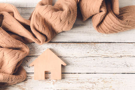Figure of house and warm scarf on wooden background. Concept of heating seasonの写真素材