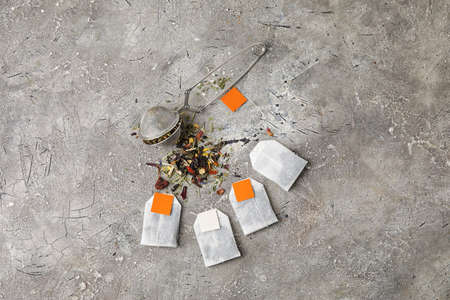 Tea bags and dry herbs on gray background