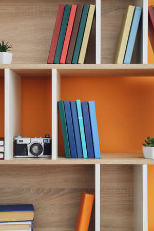 Shelf unit with books and decor on color background