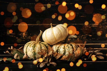 Autumn composition with pumpkins and fallen leaves on dark wooden background with blurred lightsの写真素材