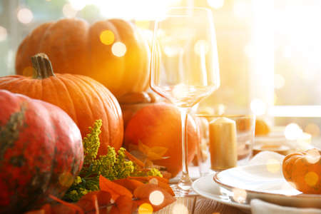 Beautiful table setting with pumpkins and autumn leaves in dining roomの写真素材