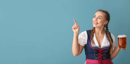 Young Oktoberfest waitress with beer pointing at something on blue background with space for textの写真素材