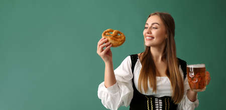Beautiful Oktoberfest waitress with beer and pretzel on green background with space for textの写真素材