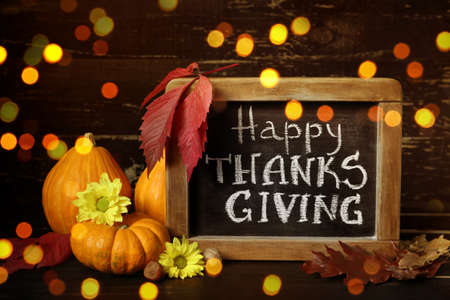 Chalkboard with text HAPPY THANKSGIVING and autumn decor on dark wooden background with blurred lightsの写真素材