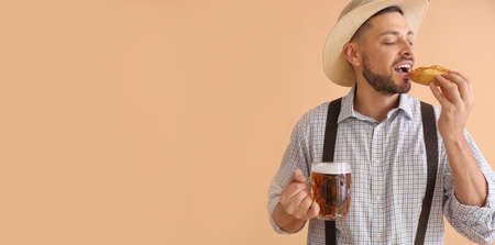 Young man in traditional German clothes with beer eating pretzel on beige background with space for textの写真素材