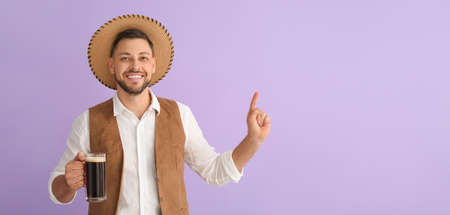 Young man in traditional German clothes with beer pointing at something on lilac background with space for textの写真素材