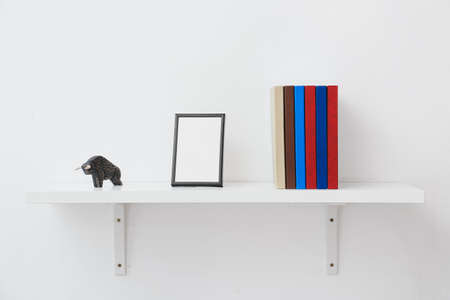 Shelf with books and blank frame on light backgroundの写真素材