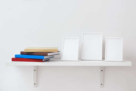 Shelf with books and blank frames on light backgroundの写真素材