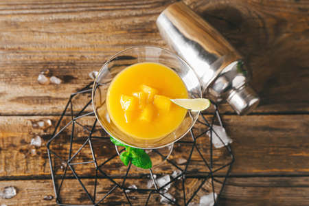 Glass of tasty mango margarita and shaker on wooden backgroundの写真素材