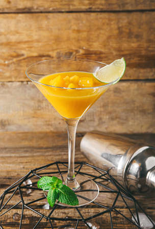 Glass of tasty mango margarita and shaker on wooden backgroundの写真素材