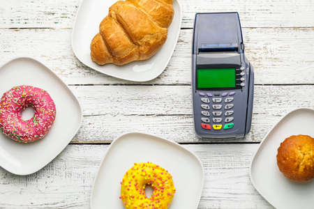 Payment terminal with donuts and croissant in plates on light wooden backgroundの写真素材