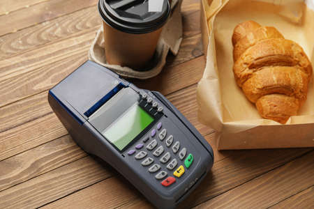 Payment terminal with takeaway cup and croissant on wooden backgroundの写真素材