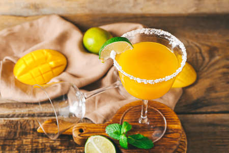 Glass of tasty mango margarita and ingredients on wooden backgroundの写真素材