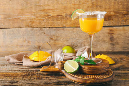 Glass of tasty mango margarita and ingredients on wooden backgroundの写真素材